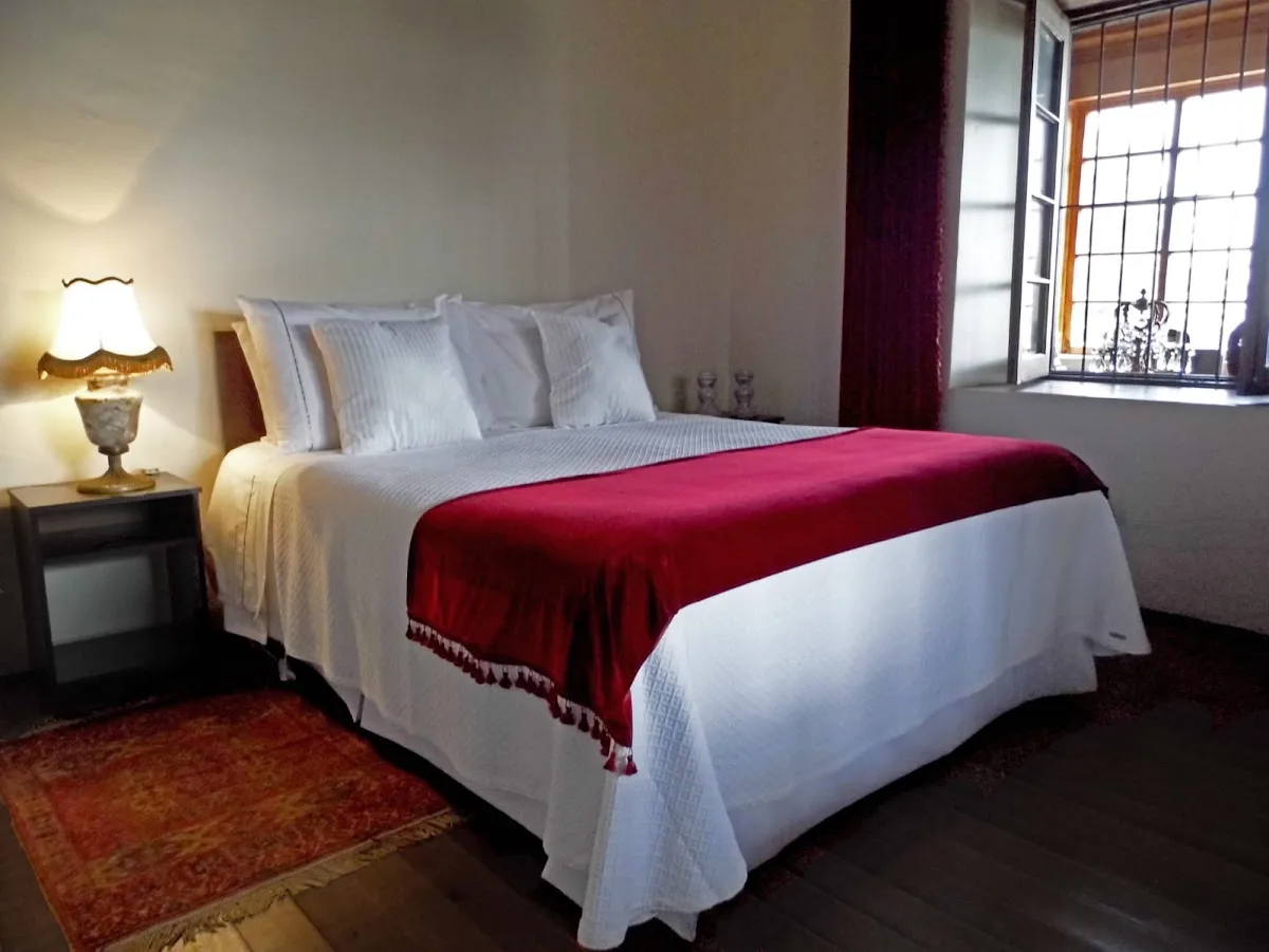Dormitorio del hotel con cama imperial de terciopelo rojo, papel mural floreado y lámparas