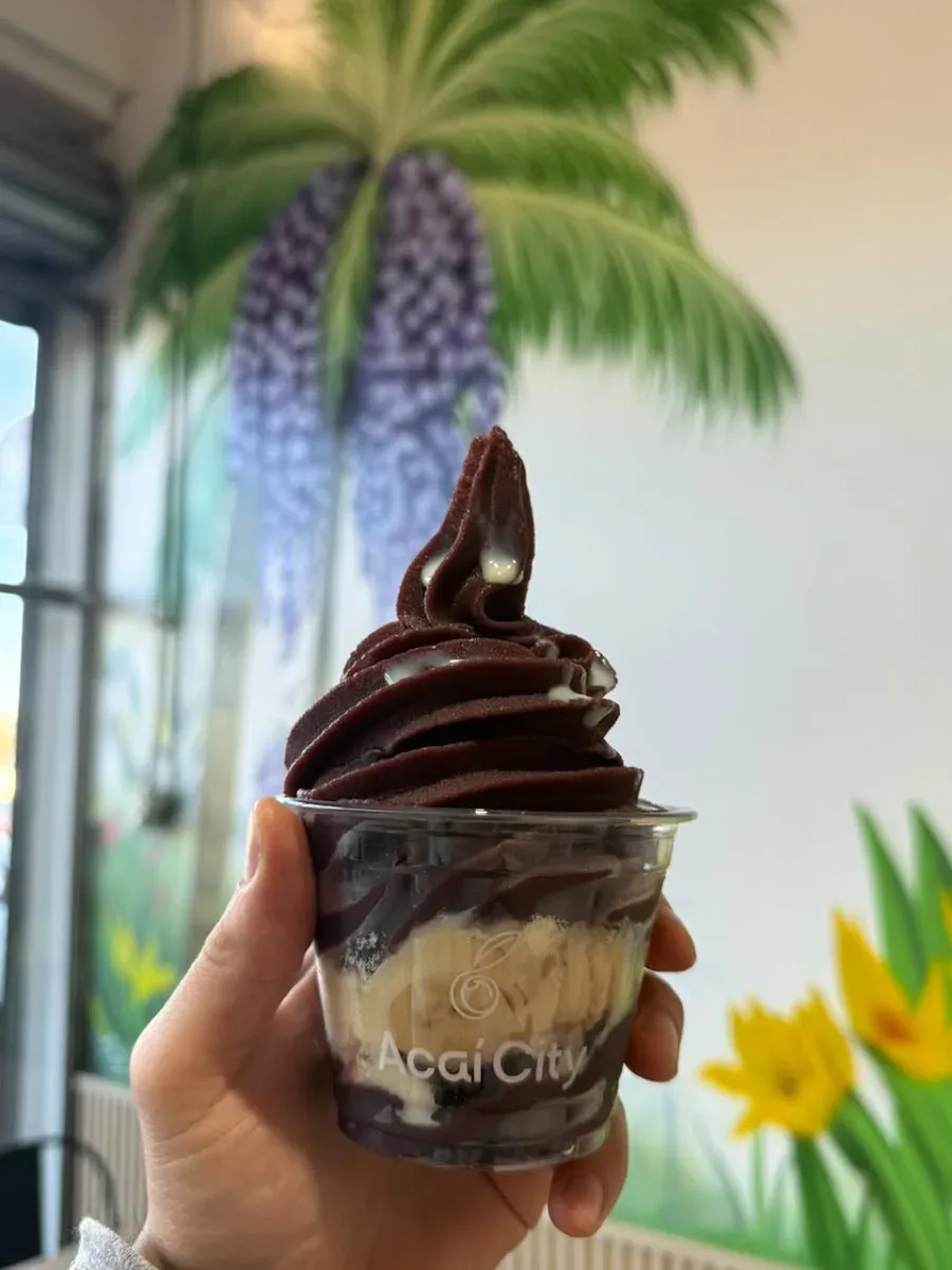 Vaso de Acai City con açaí cremoso y toppings, con el mural de fondo