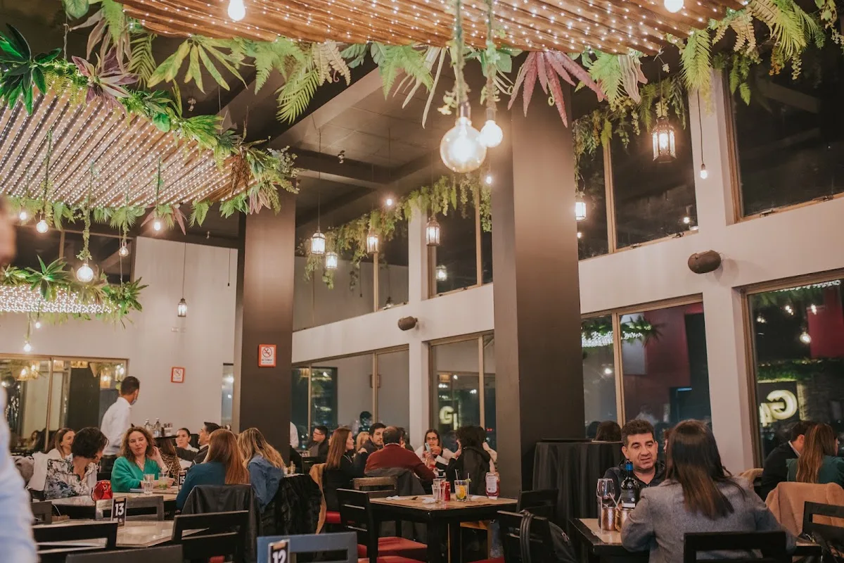Salón de Alcatorce lleno de comensales de noche, con plantas colgantes y luces cálidas