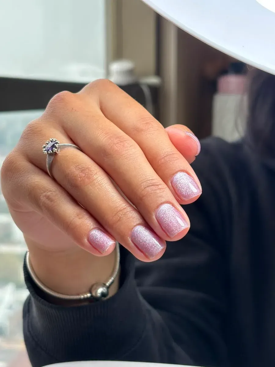 Manicura rosa glitter sobre mano de clienta con anillo