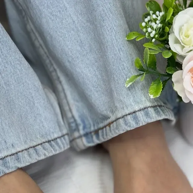 Pies de clienta con pedicura francesa, jeans y flores blancas