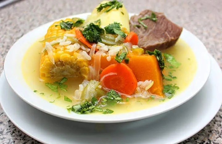 Cazuela con carne, choclo, zapallo y zanahoria servida en plato hondo
