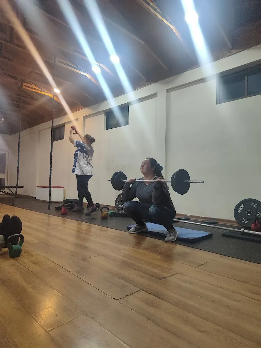 Dos alumnas entrenando: una levanta balón medicinal y otra sostiene sentadilla con barra