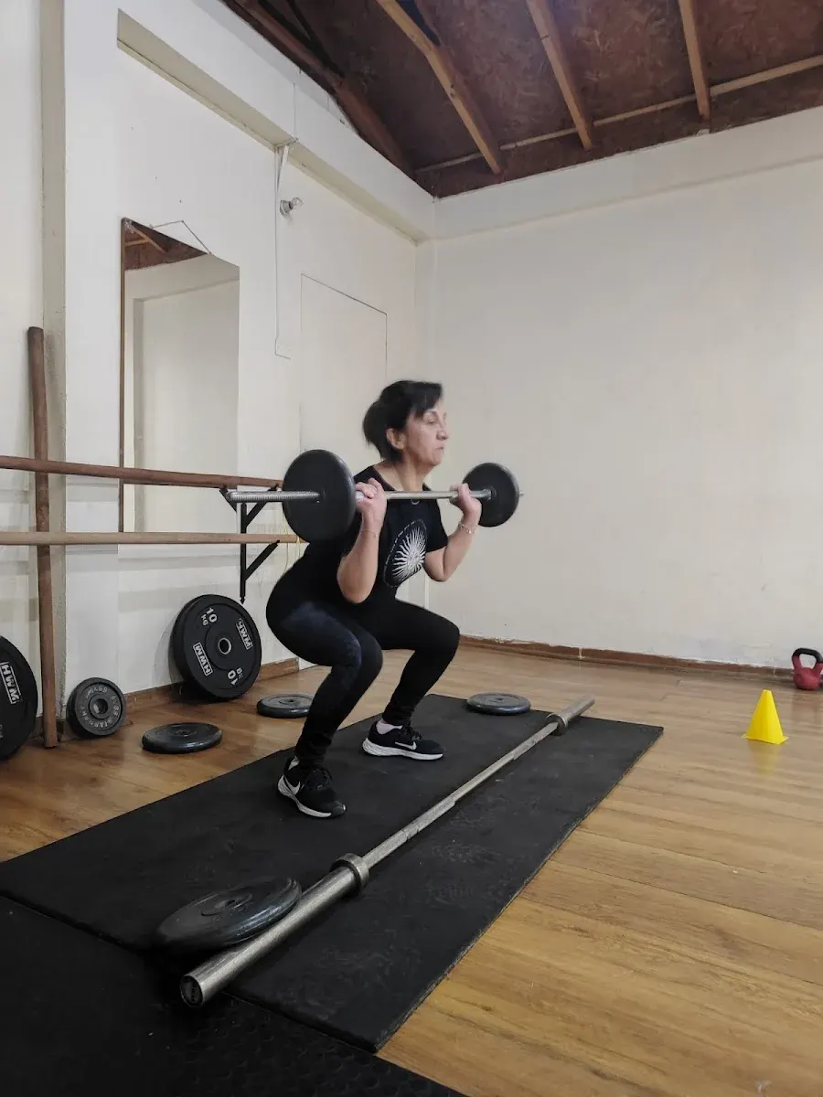 Alumna haciendo sentadilla frontal con barra en la sala de Atenas