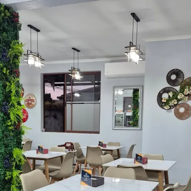 Salón de Café Baires con mesas blancas, muro de follaje verde y lámparas colgantes