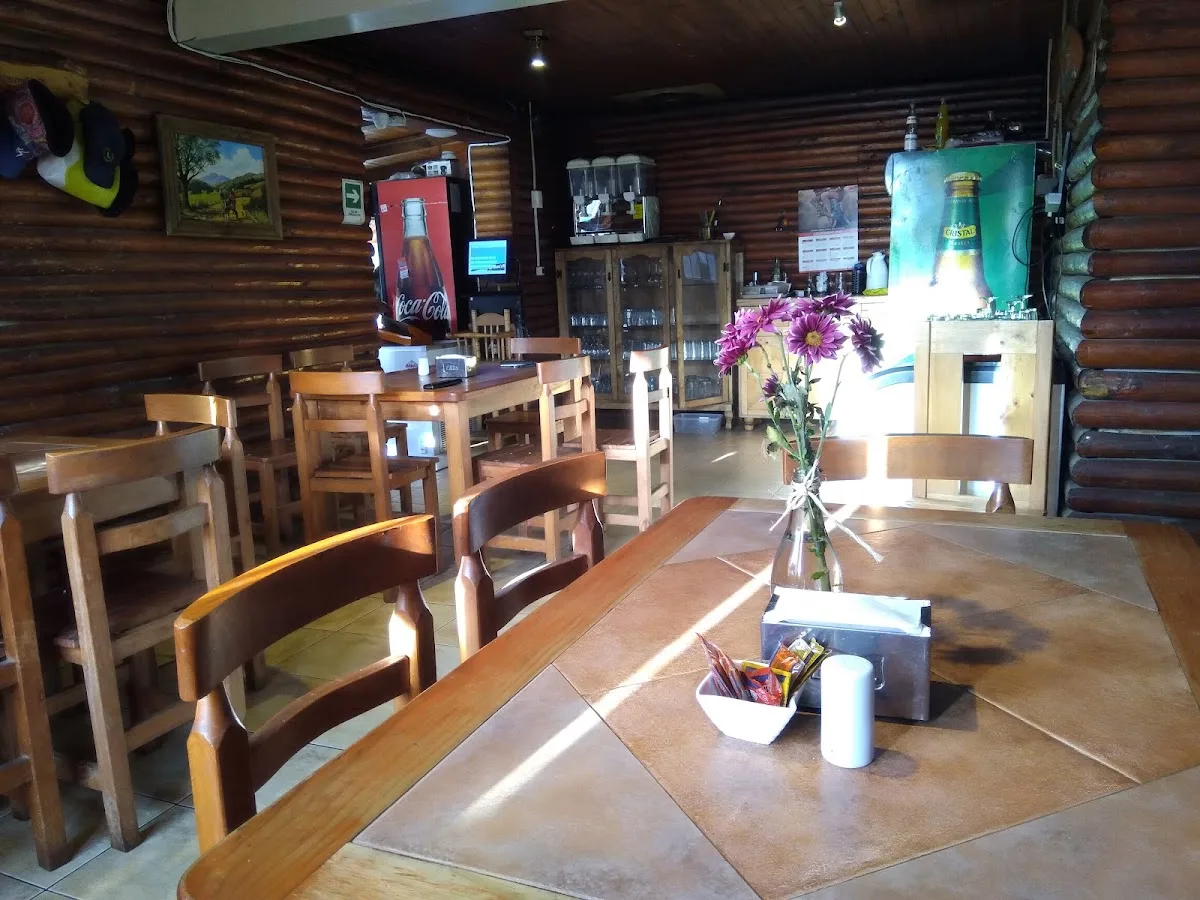 Interior real de Bruno's Bar: mesas de madera clara, paredes de troncos redondos, vitrina con copas y mesa de ping-pong al fondo