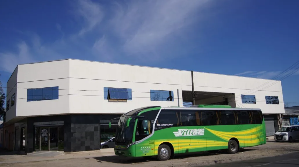 Bus verde y amarillo de Buses Villar estacionado frente a su oficina en 13 Oriente, Talca