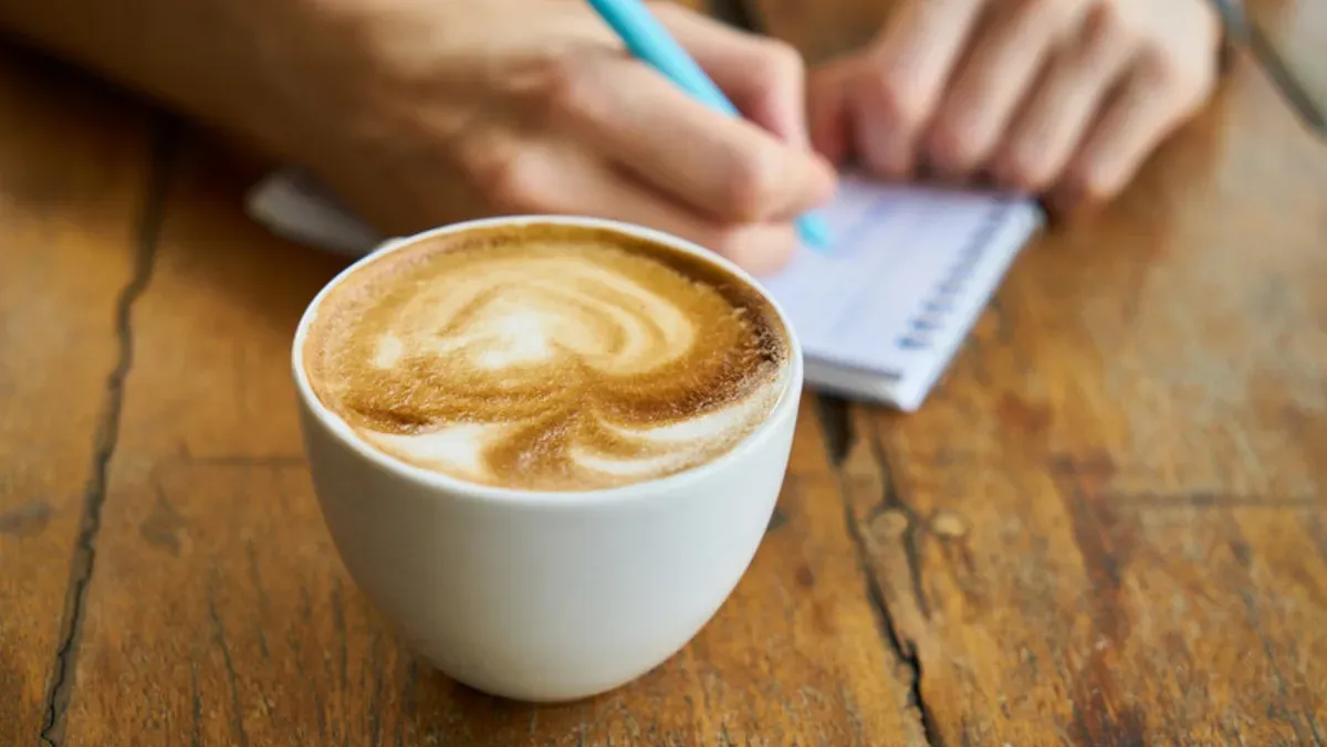 Latte art junto a un cuaderno en la mesa de Cafetería Los Nogales