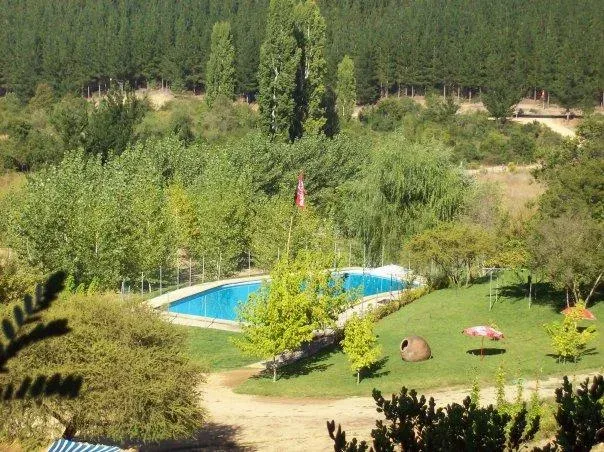 Vista aérea de Camping Entre Pinos: piscina, pradera y cerro de pinos