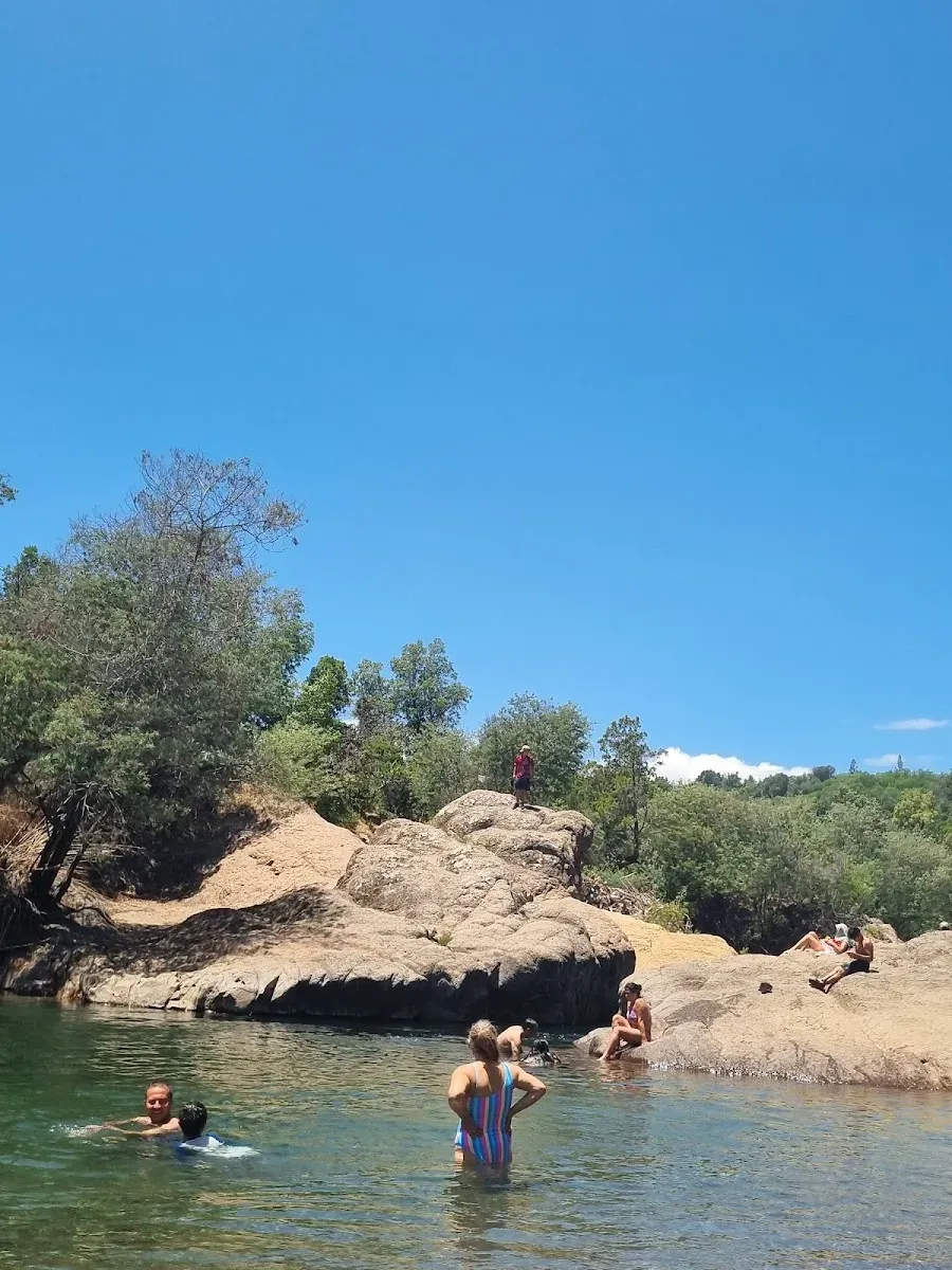 Personas bañándose junto al salto de agua entre las rocas del río