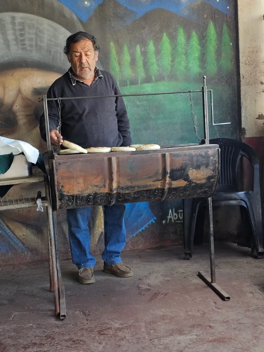 El Pelao cocinando en la parrilla del carro, con el mural pintado detrás