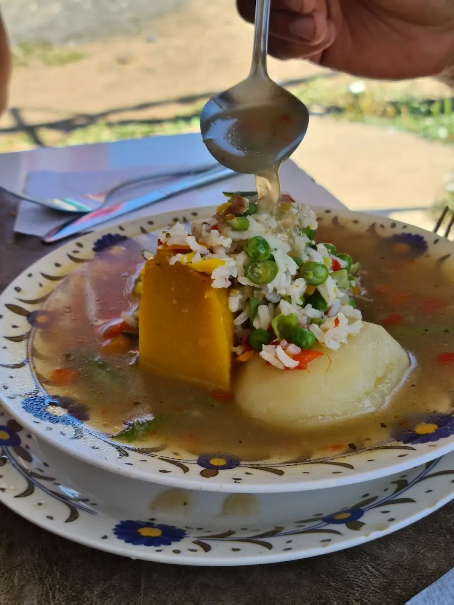 Cuchara sirviendo caldo sobre una cazuela con zapallo, papa y arvejas
