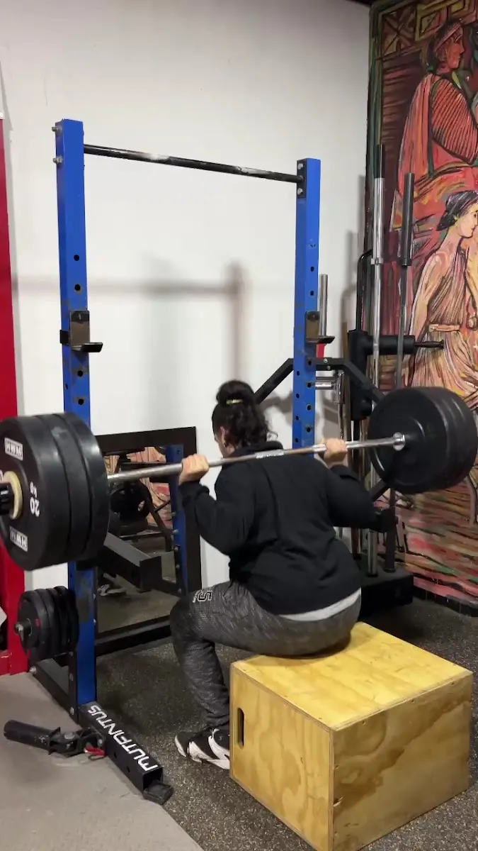 Alumna de Kaizen haciendo sentadilla con barra en el rack del dojo