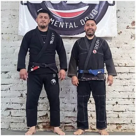 Profesores de Kaizen Grappling Arts con gi negro frente al lienzo del dojo