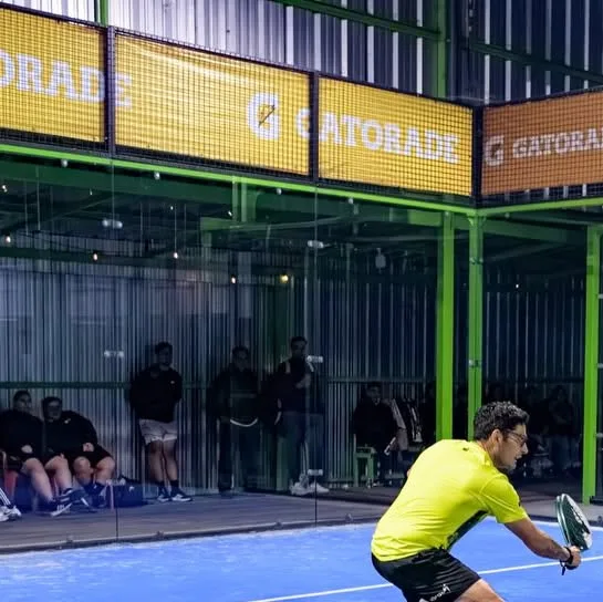 Cancha techada de pádel de Cetty: alfombra azul, estructura verde lima, muros de vidrio y banners Gatorade