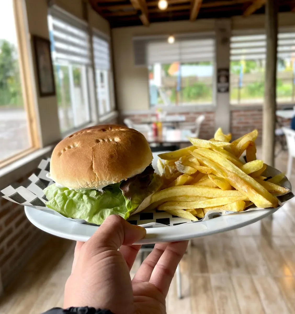Hamburguesa con papas fritas servida en la mano, en Delicias Zambelli