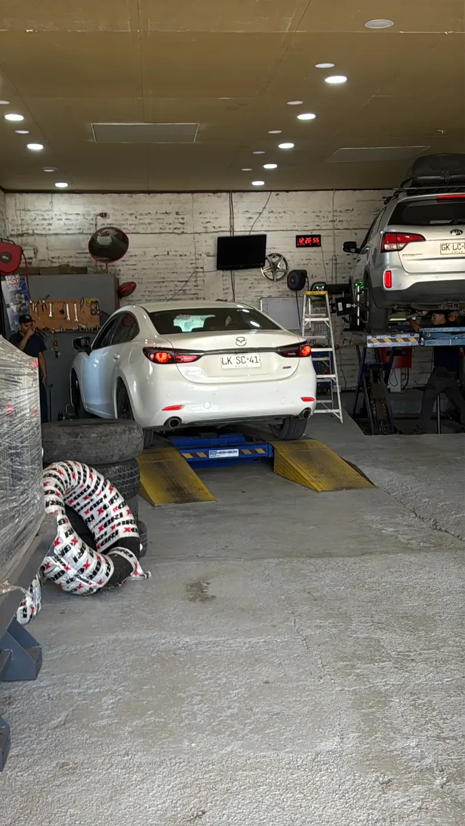 Interior del taller Direcar: dos autos en elevadores y estanterías de neumáticos