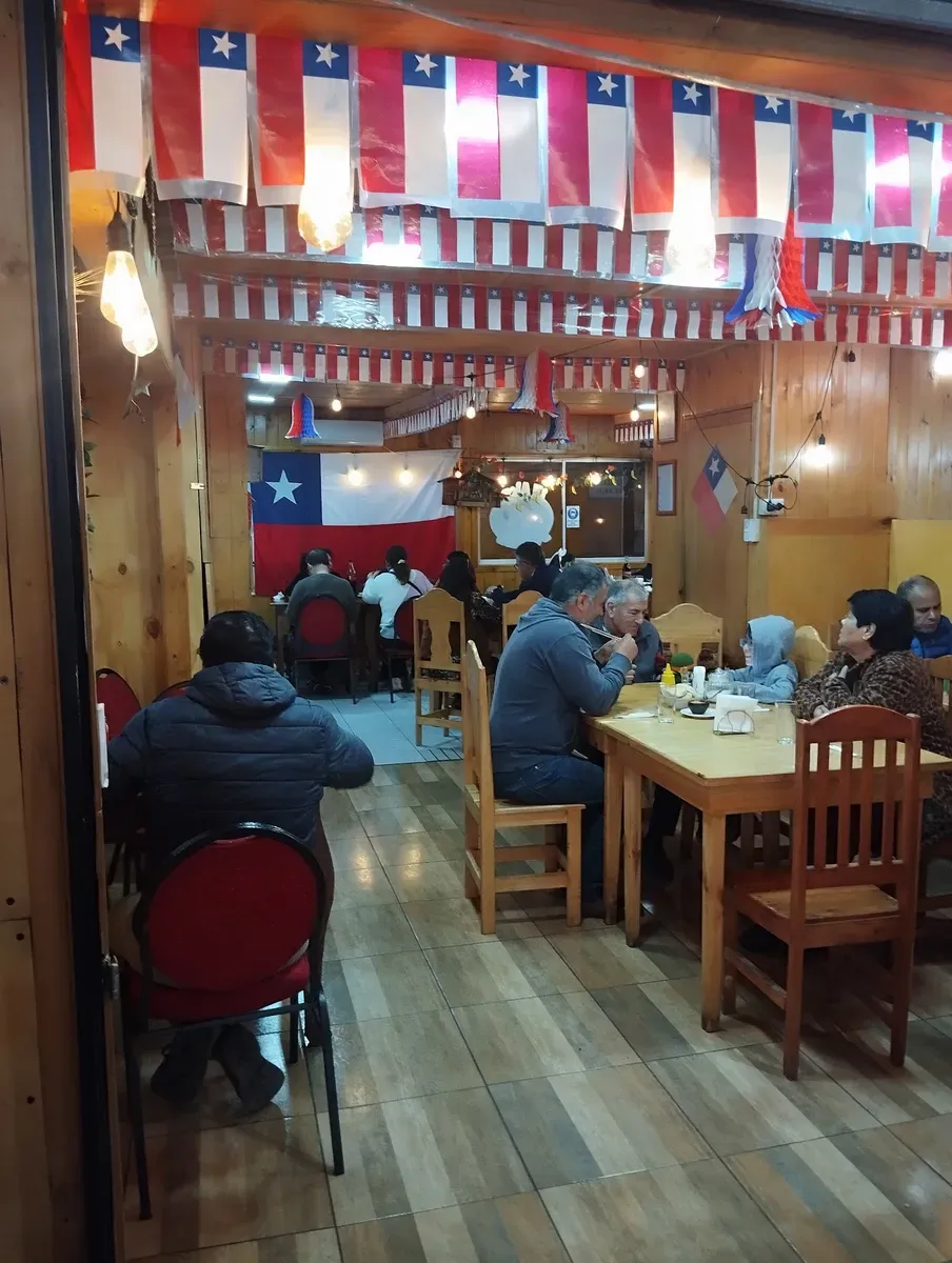 Comedor de madera de El Alero de Anita con banderas chilenas colgando del techo y mesas con comensales