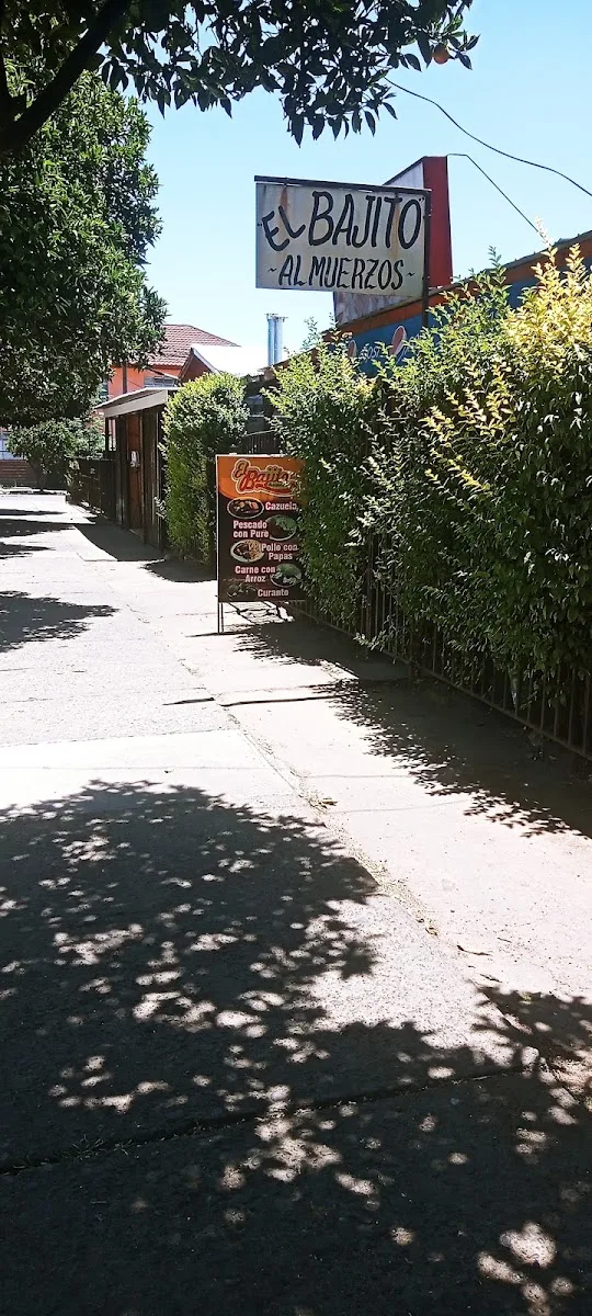 Vereda con el letrero colgante de El Bajito Almuerzos y la carta del día