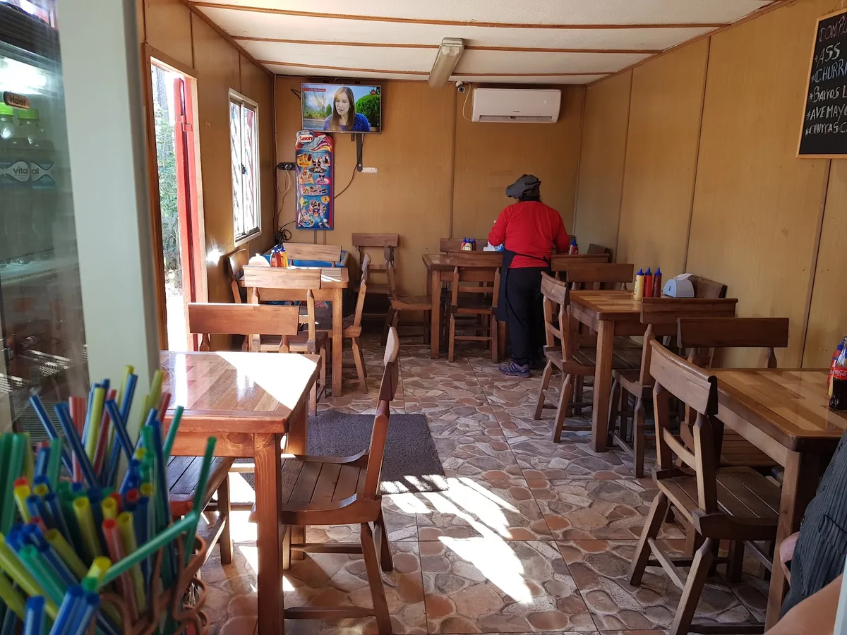 Comedor de El Bajito con mesas de madera, televisión y cocina atendida por su dueña