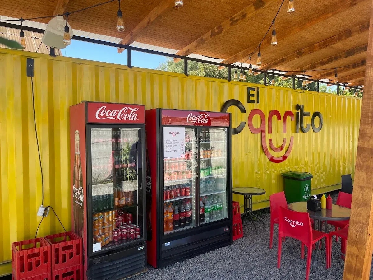 Terraza de El Carrito con mesas rojas frente al container amarillo