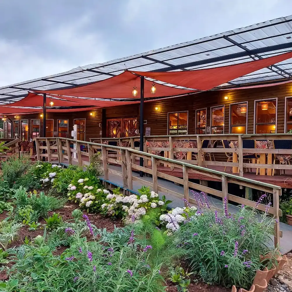 Fachada de madera con tejado rojo y jardines florales frente a El Quincho de Pelluhue