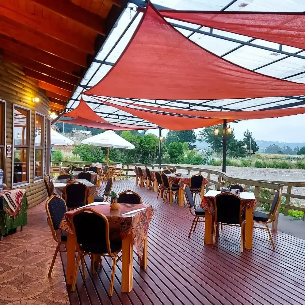 Terraza techada de madera con manteles, toldo rojo y vista a la orilla del agua en El Quincho de Pelluhue