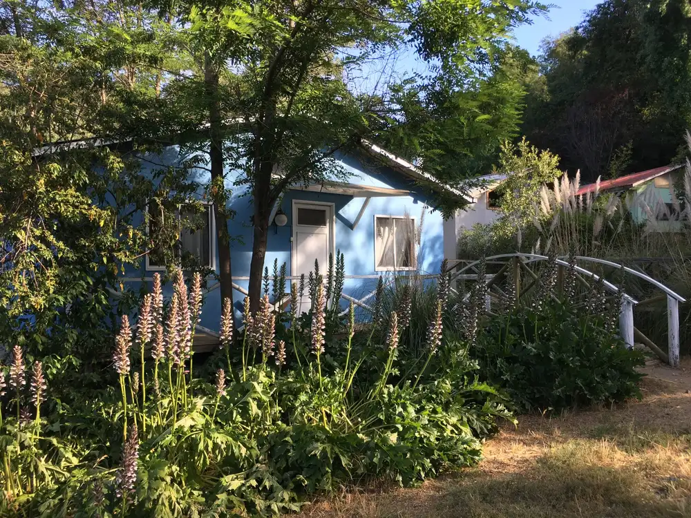 Cabaña azul del Complejo Turístico El Roble rodeada de jardín y árboles nativos