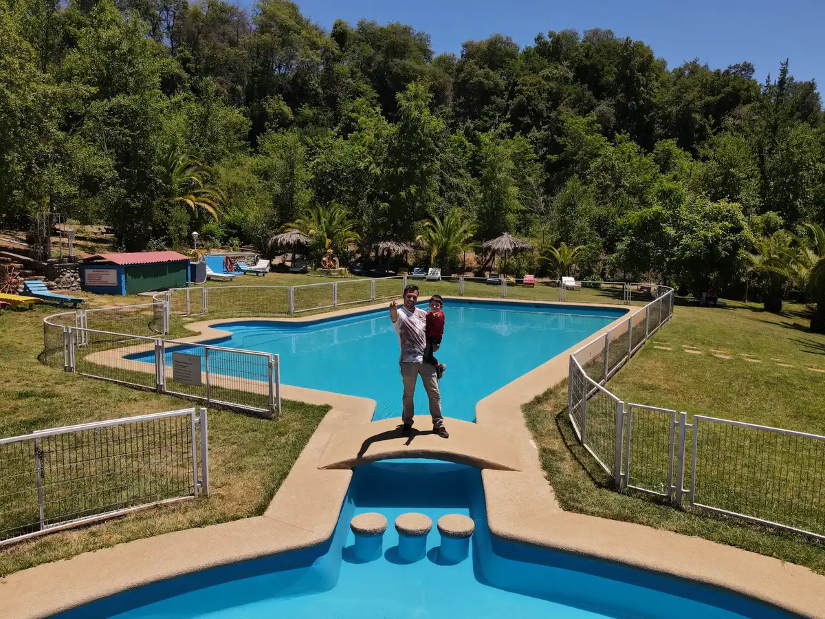 Vista aérea del Complejo Turístico El Roble: dos piscinas turquesa, cabañas y bosque nativo junto a la ruta