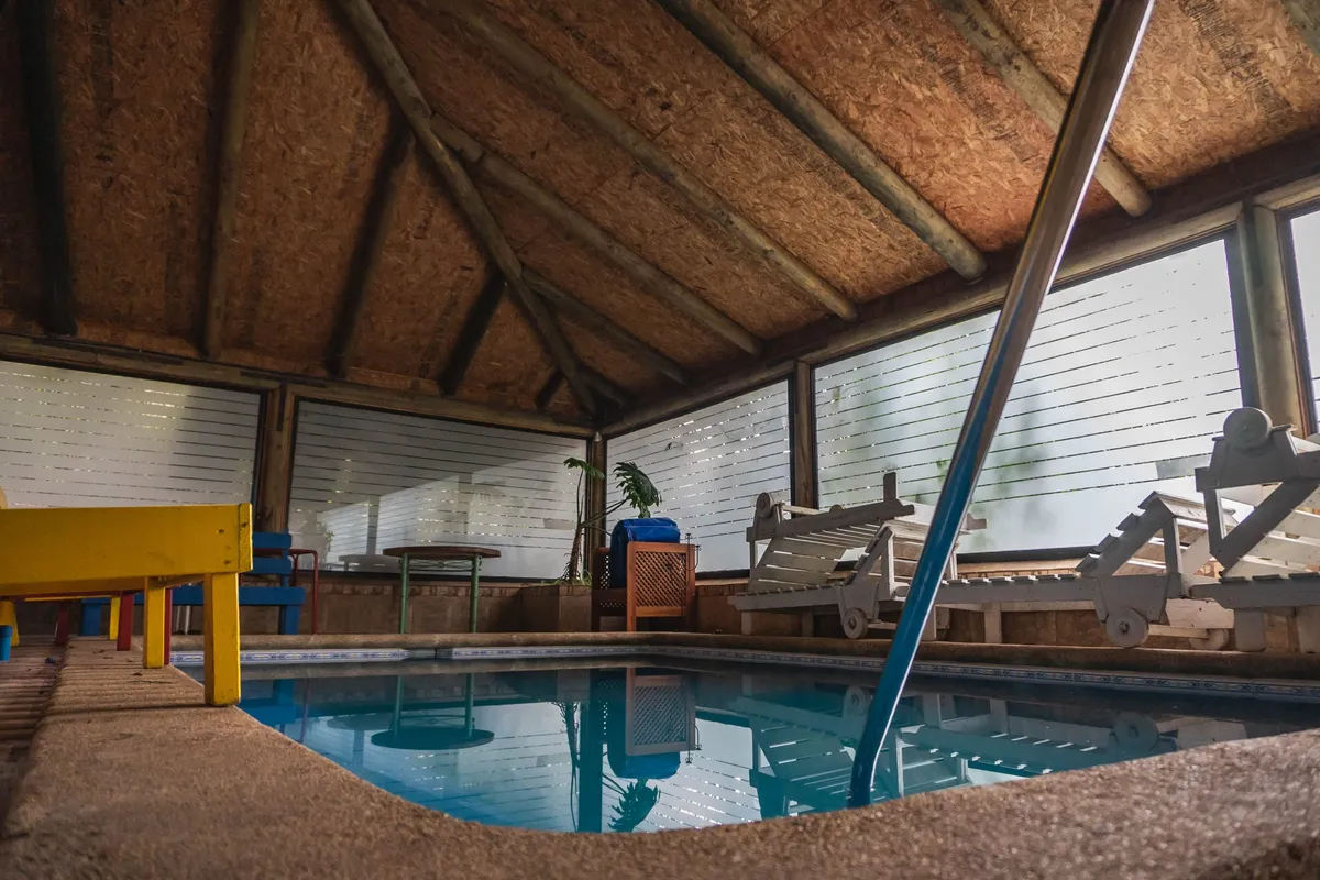 Piscina cubierta dentro del quincho con reposeras y techo de madera
