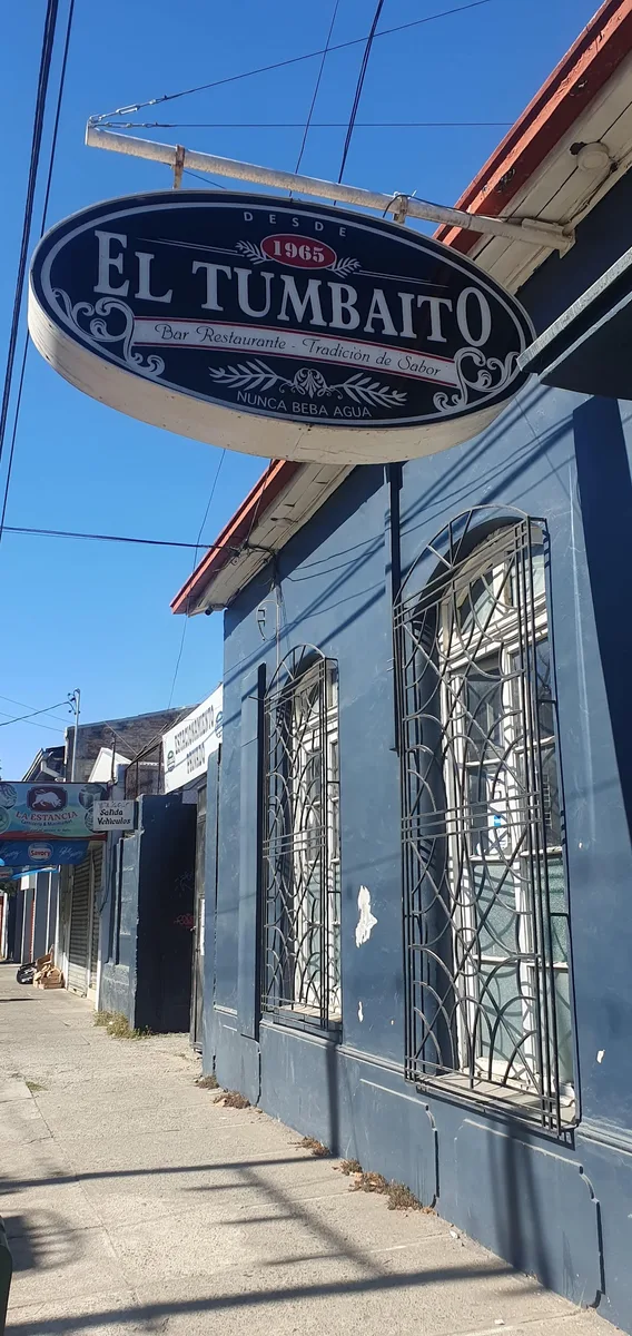 Letrero ovalado de El Tumbaito colgado en la fachada azul: 'Bar Restaurante, tradición de sabor, desde 1965, nunca beba agua'