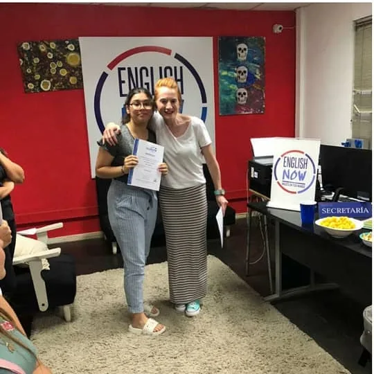Dos alumnas con certificado frente al logo circular de English Now