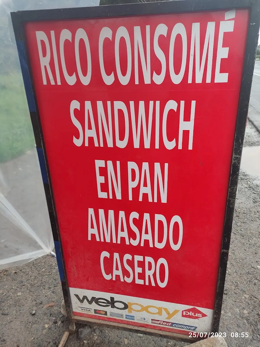 Letrero rojo de pie junto a la ruta: «Rico consomé, sandwich en pan amasado casero»