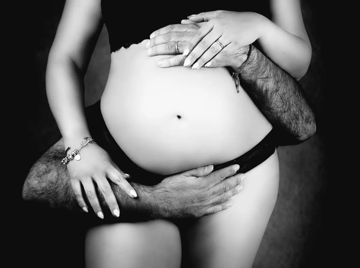 Primer plano en blanco y negro de las manos de una pareja abrazando la guatita de embarazo