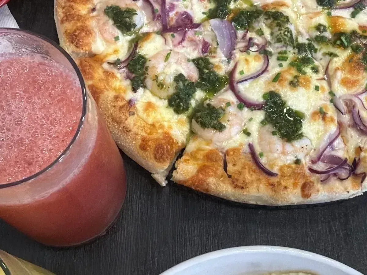 Pizza De La Costa de Frontera con camarones y palta junto a un jugo natural