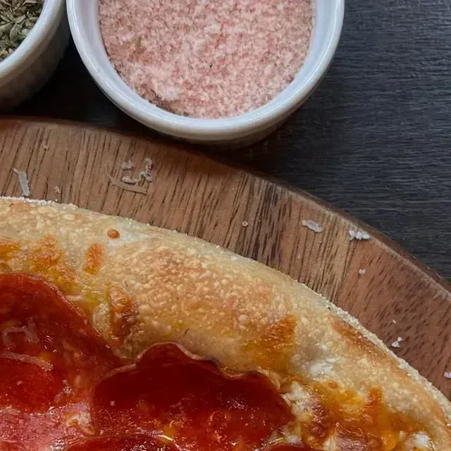 Pizza artesanal de Frontera recién salida, con un pocillo de merkén al lado