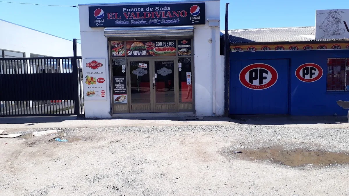 Fachada de la Fuente de Soda El Valdiviano en Av. Dr. Meza, Cauquenes: letrero azul con el nombre en rojo y vinilos de la carta en el ventanal