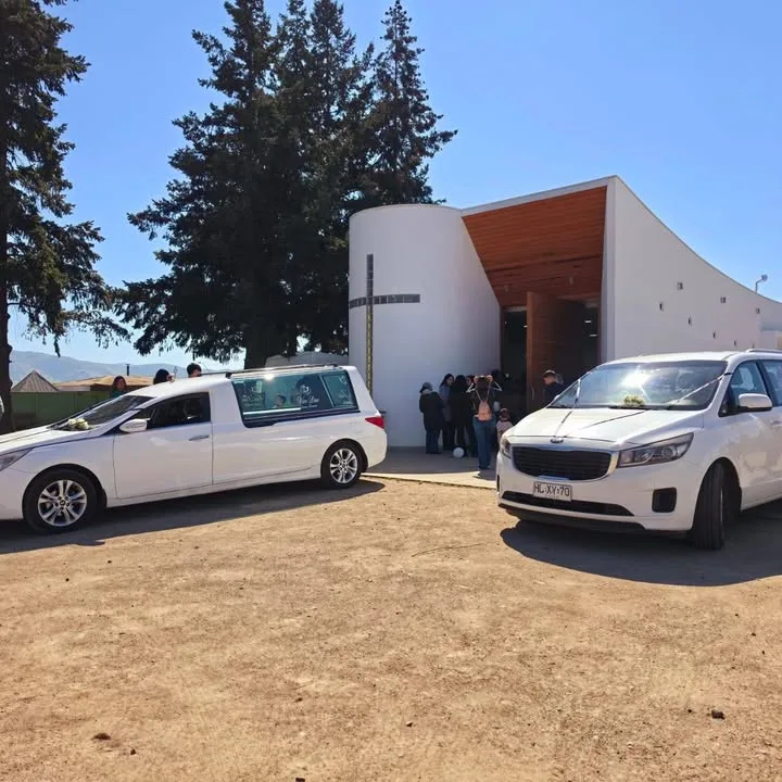Carroza fúnebre blanca estacionada en la entrada de una capilla con cruz