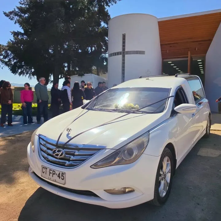 Carroza fúnebre Hyundai blanca frente a la capilla del cementerio