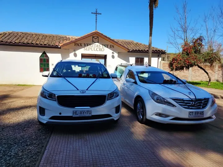 Dos carrozas funebres blancas de Funeraria Vive Dios frente a la capilla del cementerio