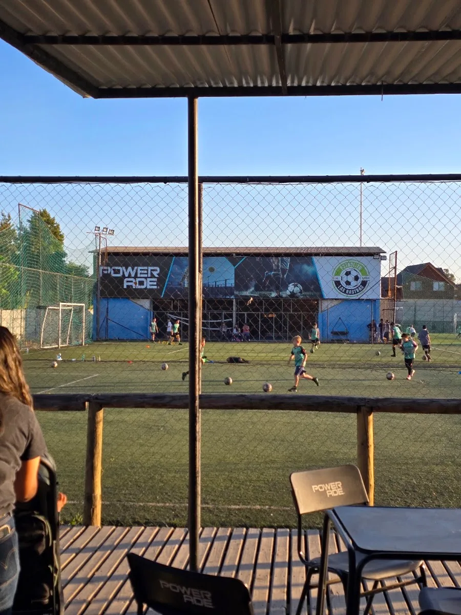 Cancha de futbolito de pasto sintético de Las Rastras al atardecer, con el mural del recinto y la terraza de la cafetería