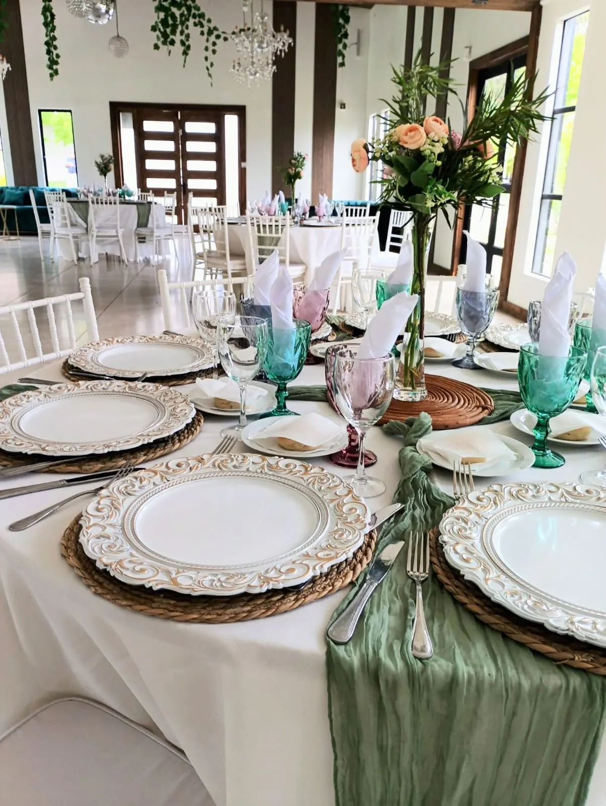 Mesa de salón con platos de borde dorado, copas de color y camino de mesa verde