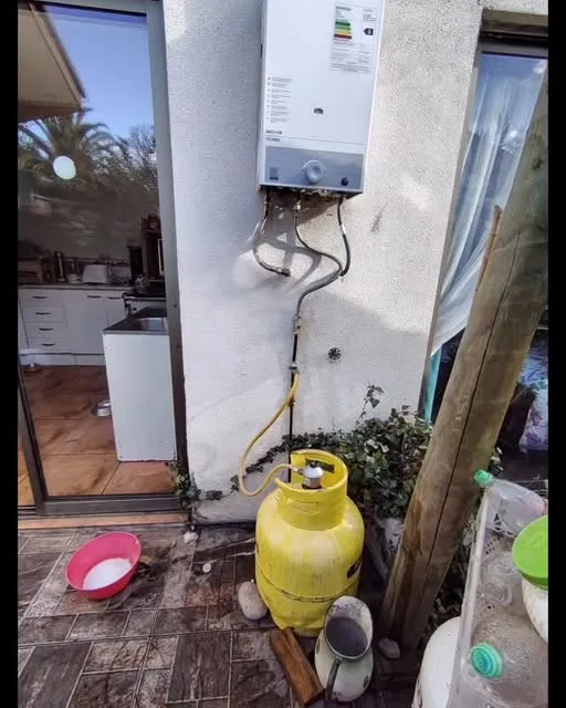 Calefont mural junto a cilindro de gas amarillo, instalación exterior de Tecnifem