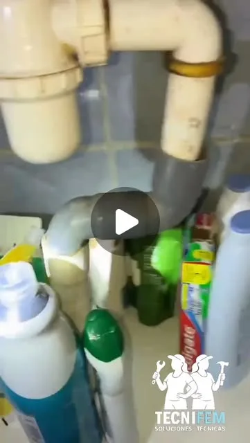 Tuberías y sifón bajo un lavamanos con productos de limpieza al lado