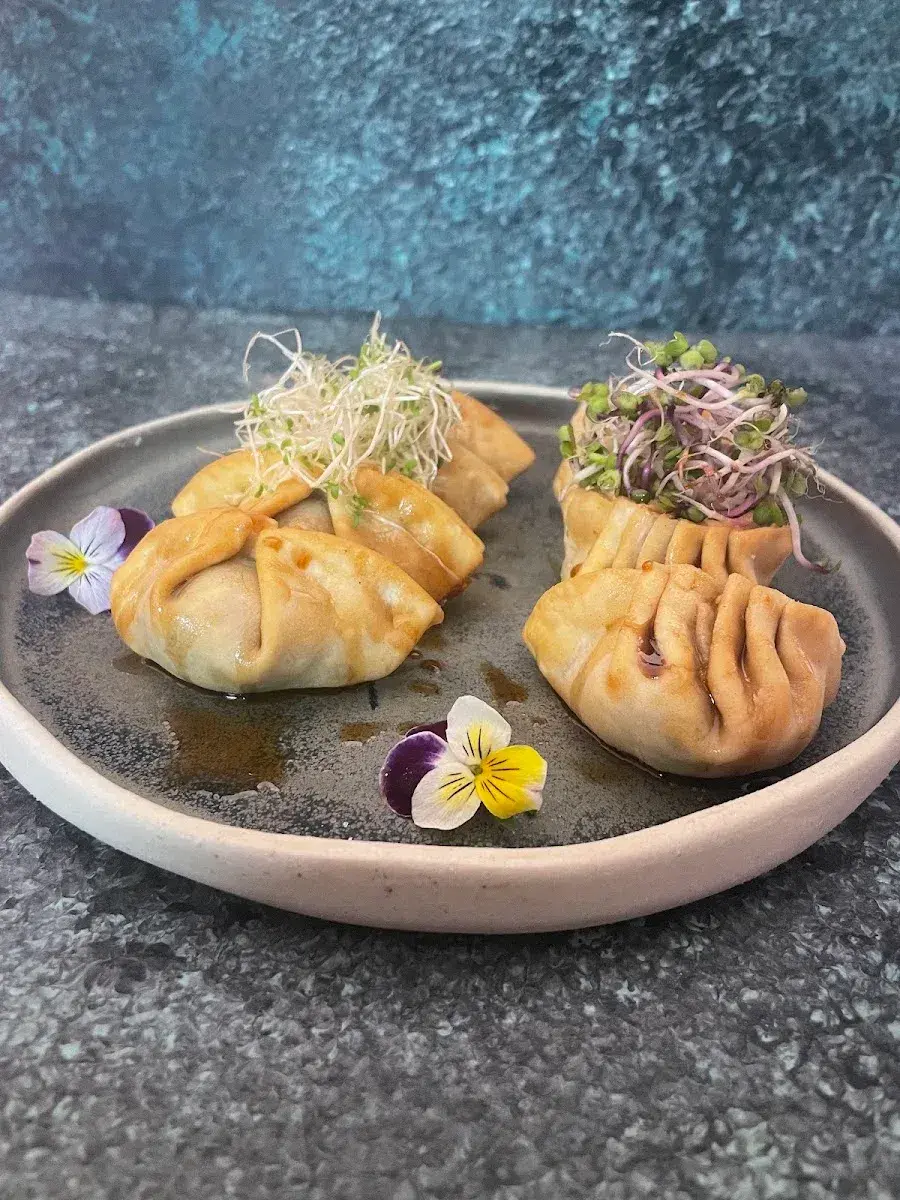 Gyozas doradas servidas en plato oscuro con brotes y flores comestibles