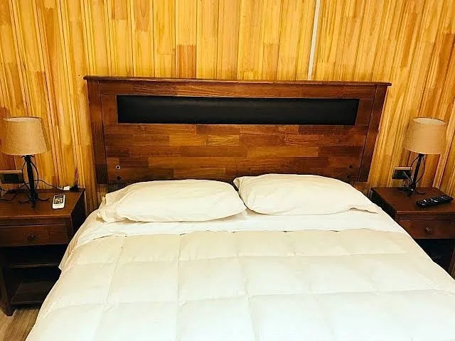 Cama con cubrecama blanco sobre muro revestido en madera clara