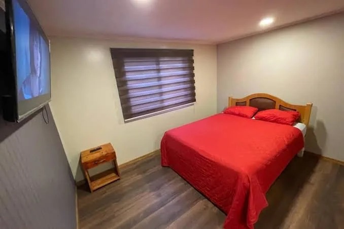 Habitación con cama de cubrecama rojo y velador de madera