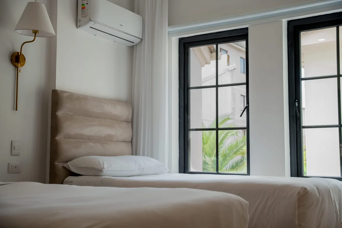 Habitación matrimonial king con ropa de cama blanca, espejo dorado y lámpara de pie