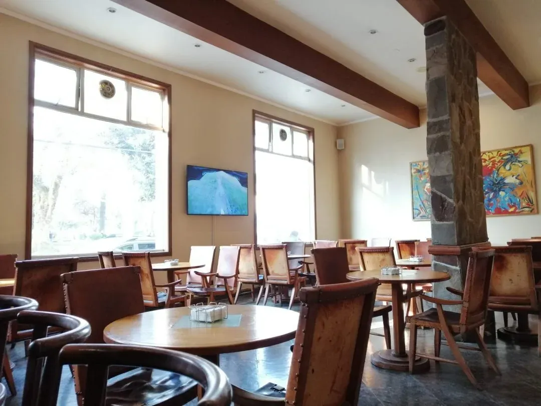 Bar cafetería del hotel con sillones de cuero y mesas redondas junto a ventanales