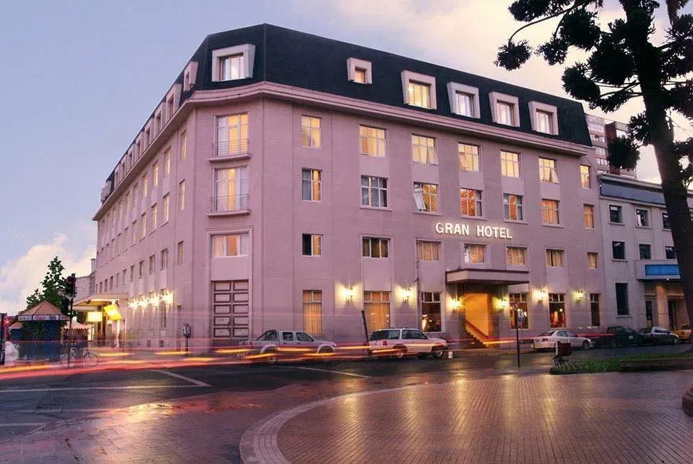 Fachada del Gran Hotel Isabel Riquelme al atardecer, con las ventanas encendidas frente a la Plaza de Armas de Chillán